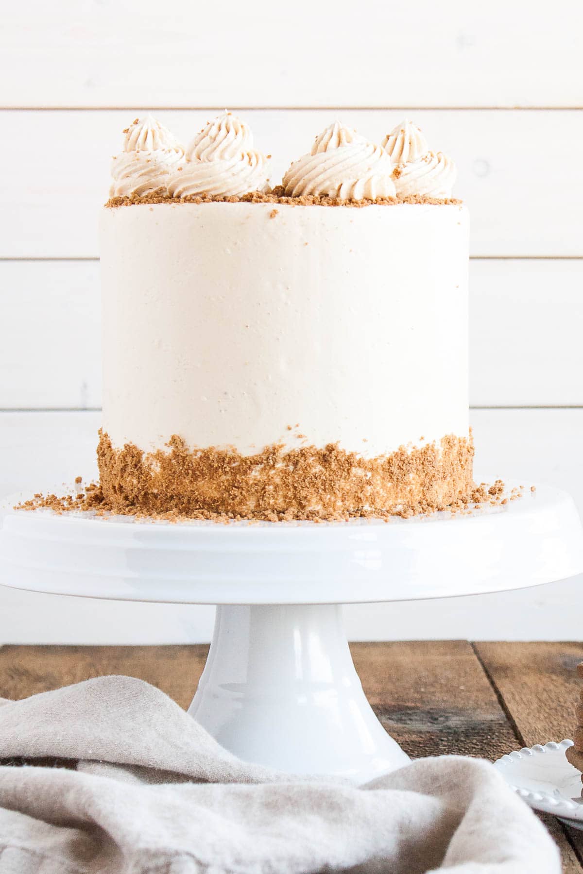 This Biscoff Cake pairs fluffy vanilla cake layers with a sweet cookie butter frosting and crushed speculoos cookies. | livforcake.com Straight on shot of the cake on a white cake stand and a white background.