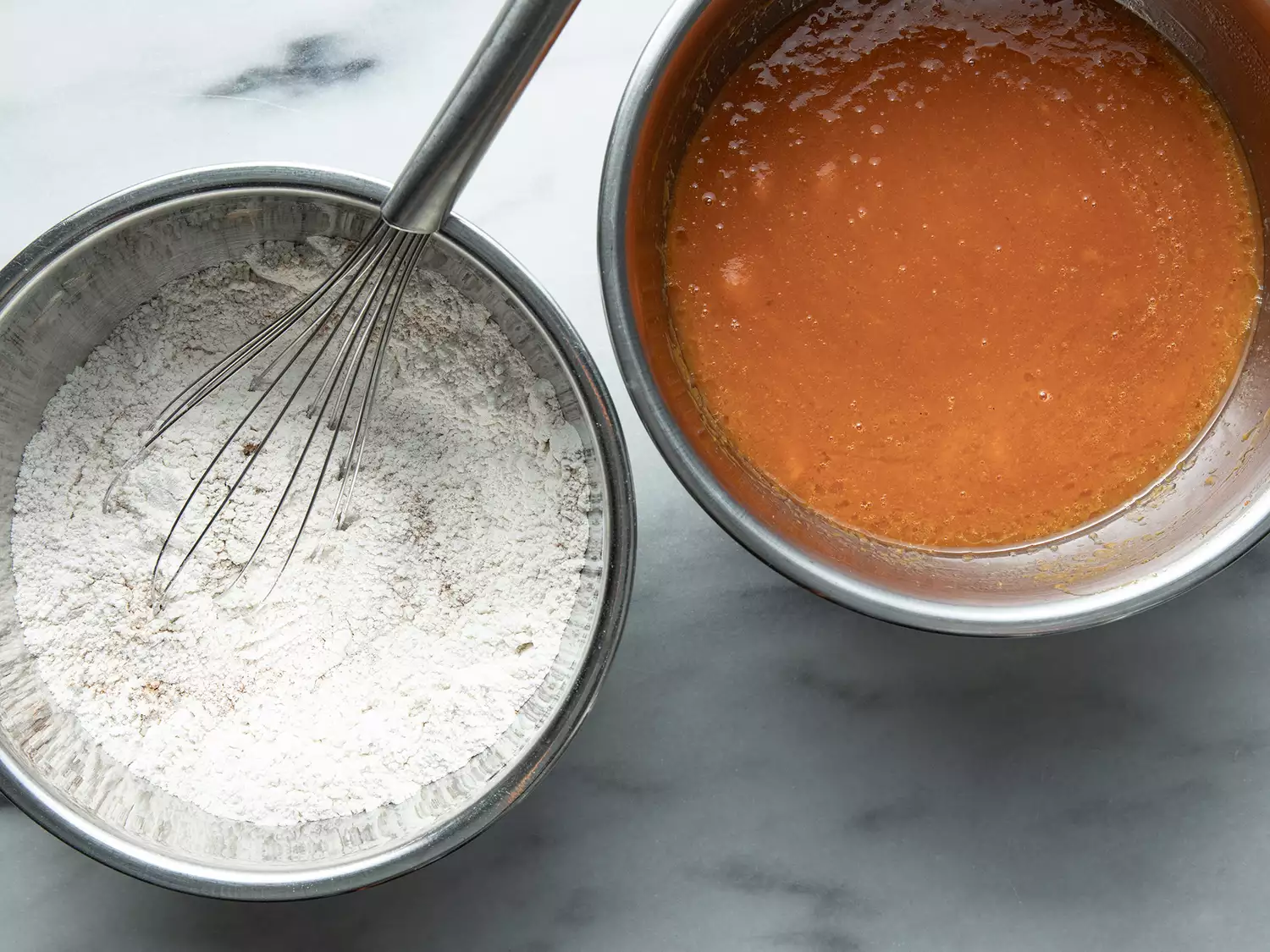 Overhead of a bowl with a flour mixture and a whisk in it and a bowl with a pumpkin mixture in it. 