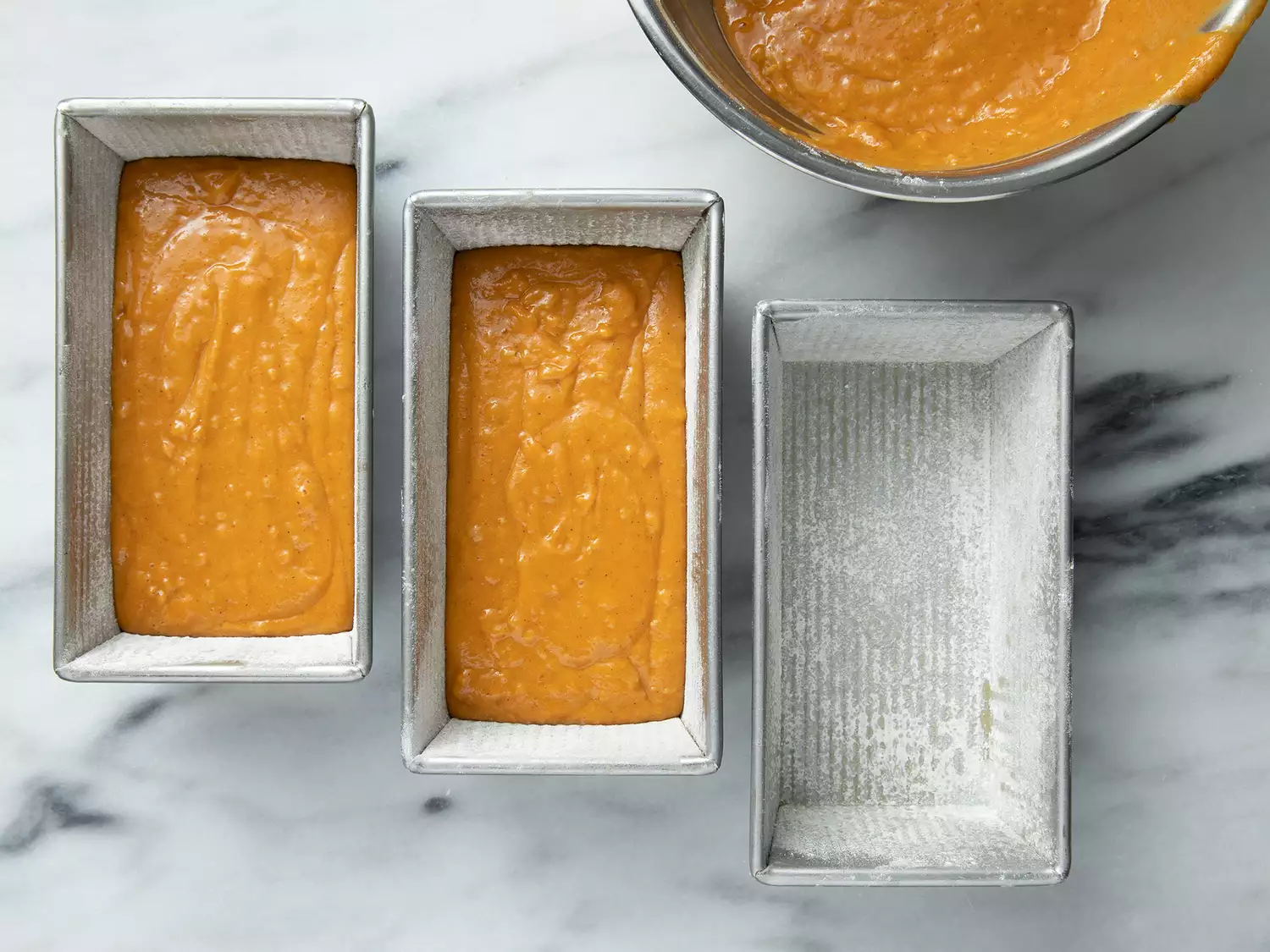 Overhead of a pumpkin batter being poured into three bread pans. 