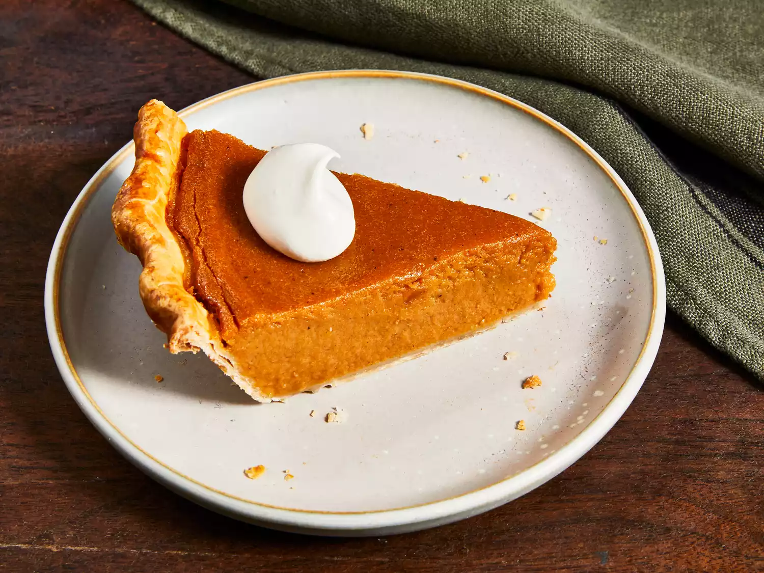 close up on a single serving of sweet potato pie on a plate, topped with whipped cream